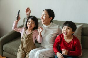 excited young ethnic woman with kids watching funny cartoon on tv