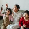 excited young ethnic woman with kids watching funny cartoon on tv